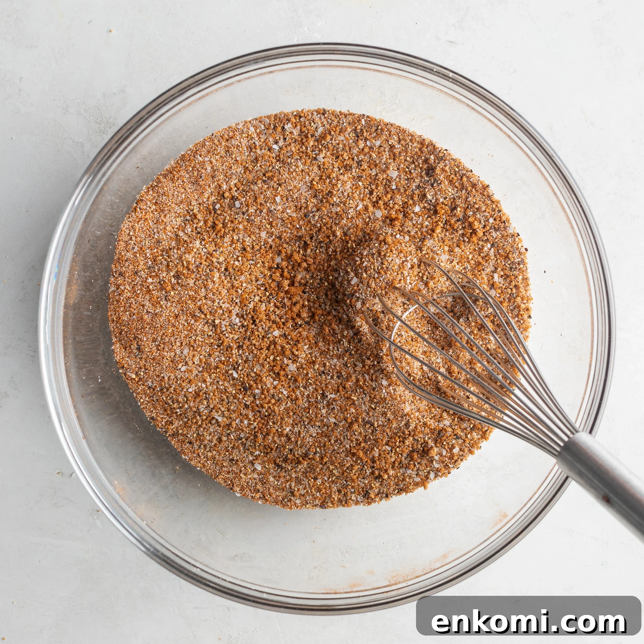 Homemade BBQ Rub Recipe for Tender, Flavorful Grilling 6 BBQ seasoning in a large glass mixing bowl with a whisk.