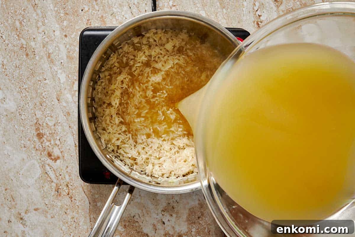 Garlic Butter Rice Recipe: Fluffy, Flavorful Side Dish 6 pot on a stove with garlic, butter and rice having stock being poured in