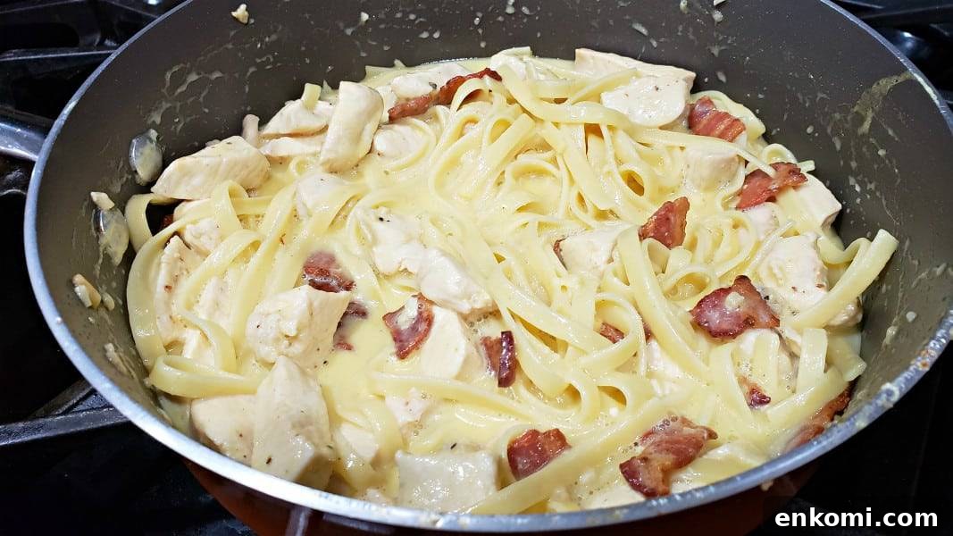 diced chicken, pasta, bacon, and parmesan sauce cooking in a large pan for this Chicken Carbonara recipe.