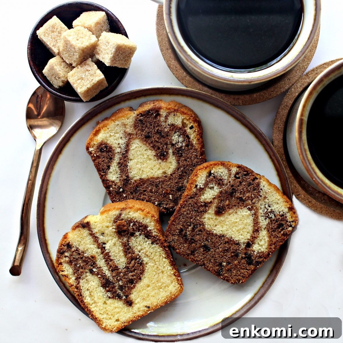 Three slices of marbled cake on a plate next to two cups of coffee.