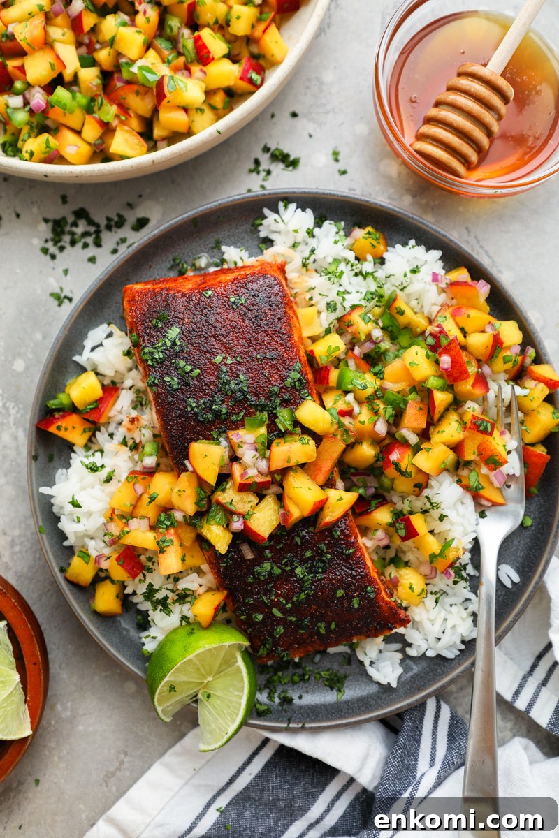 A plate serving white rice with roasted chipotle salmon and fresh peach salsa surrounded by a bowl of peach salsa and a smaller jar of honey