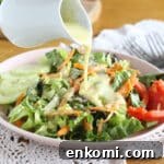 Plate full of lettuce and raw vegetables with a dressing being poured over the top.