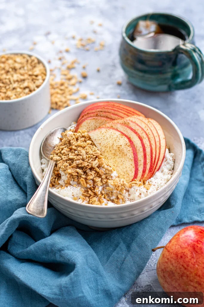 Cottage Cheese & Apple Breakfast Bowls with Granola and Honey 3 A bowl on a blue towel, the bowl is filled with cottage cheese and topped with apple slices, granola, and dusted in cinnamon.