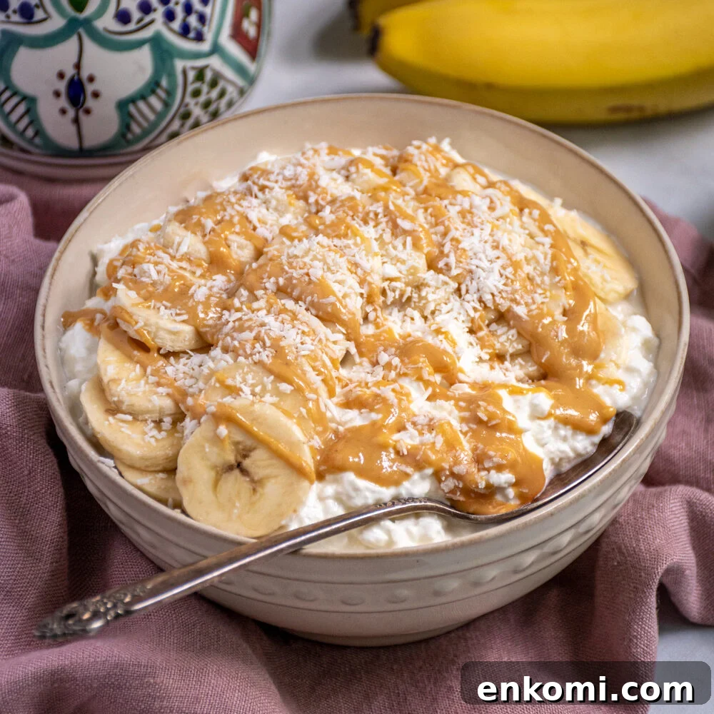 Cottage Cheese & Apple Breakfast Bowls with Granola and Honey 5 White bowl gilled with cottage cheese and topped with banana slices, peanut butter, and shredded coconut.
