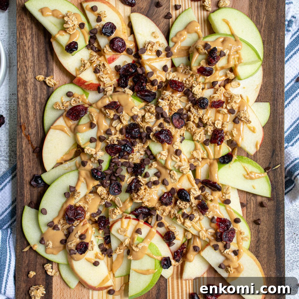 Cottage Cheese & Apple Breakfast Bowls with Granola and Honey 7 Overhead view of a wood cutting board piled high with apple slices covered in peanut butter, granola, dried cranberries, and mini chocolate chips.