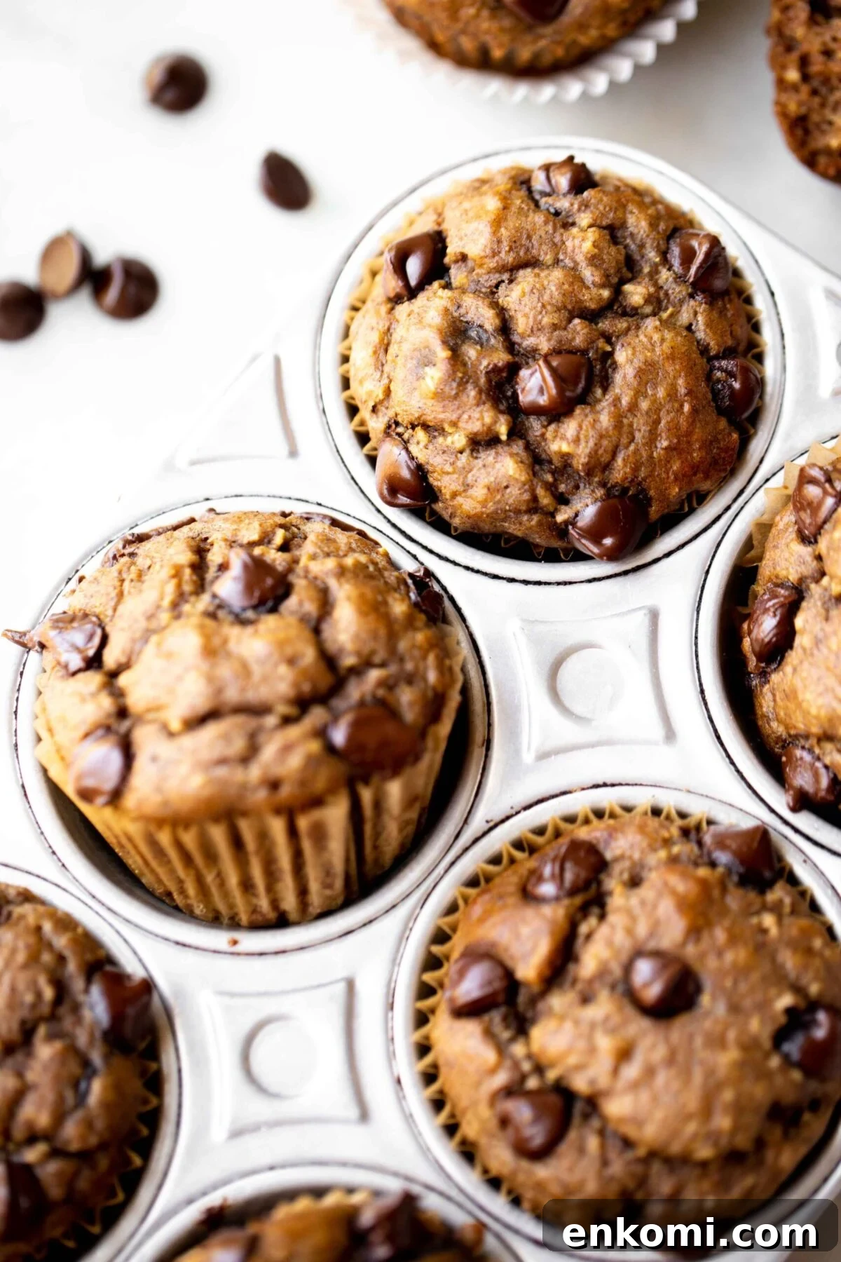Banana Lentil Muffins with Oats — Protein-Packed Snack Recipe 3 closeup photo at 45 degree angle of freshly baked chocolate chip banana muffins in an aluminum muffin pan on a light gray marble background