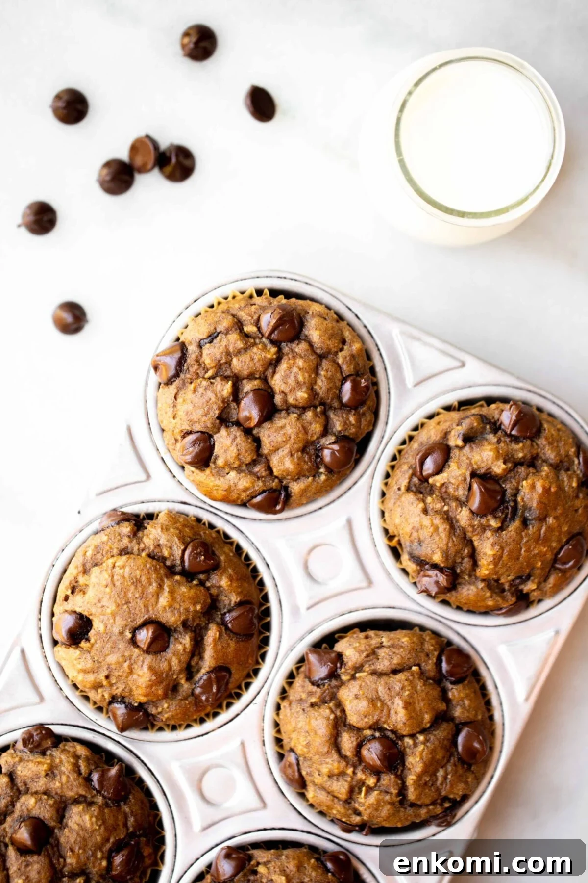 Banana Lentil Muffins with Oats — Protein-Packed Snack Recipe 4 overhead photo of freshly baked chocolate chip banana muffins in an aluminum muffin pan with milk and chocolate chips in the background