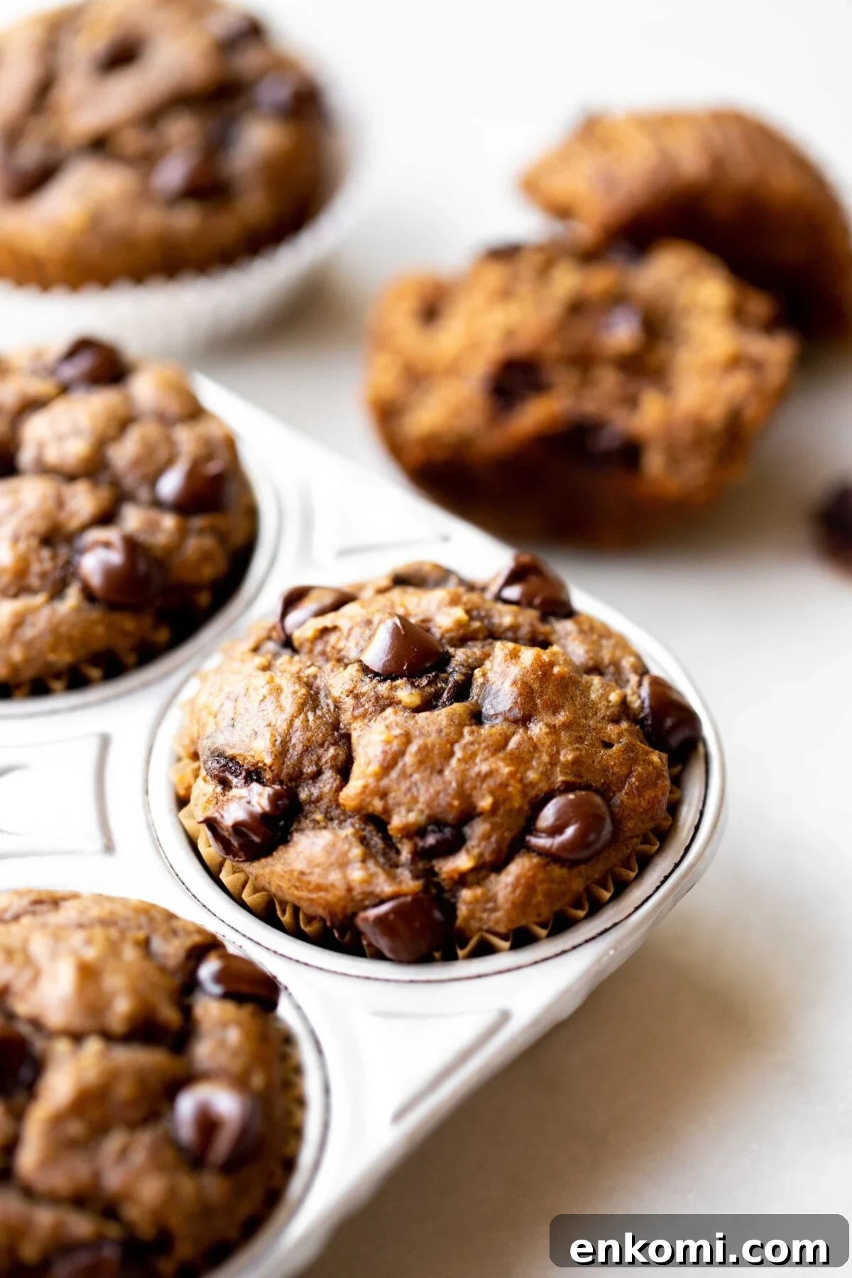 Banana Lentil Muffins with Oats — Protein-Packed Snack Recipe 5 closeup photo at 45 degree angle of freshly baked healthy chocolate chip banana muffins in an aluminum muffin pan on a light gray marble background