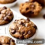 closeup photo at 45 degree angle of freshly baked healthy chocolate chip banana muffins in an aluminum muffin pan on a light gray marble background