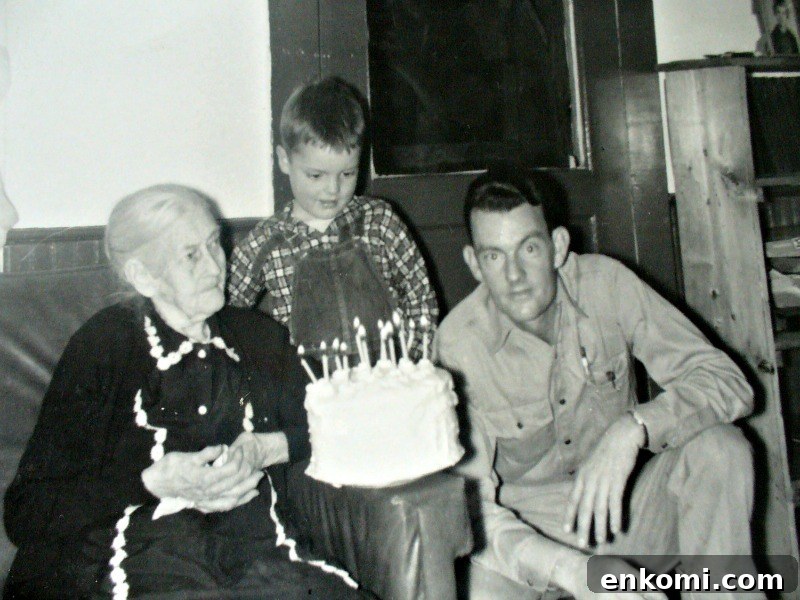 Black and white photo of elderly woman, young boy, man gathered around white birthday cake.
