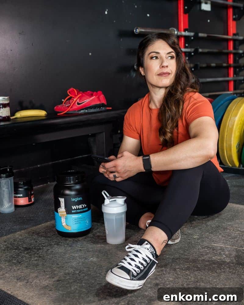 woman with brown hair sitting on a gym floor holding an iphone