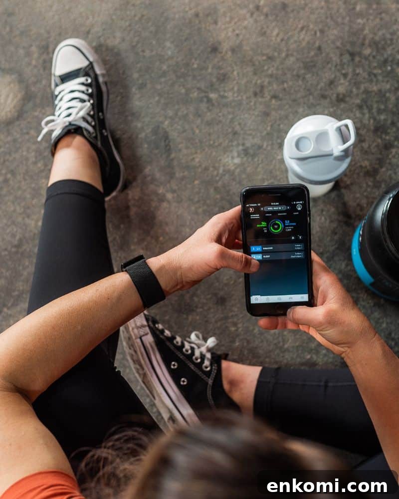 woman with brown hair sitting on a gym floor holding an iphone with the whoop recovery app open