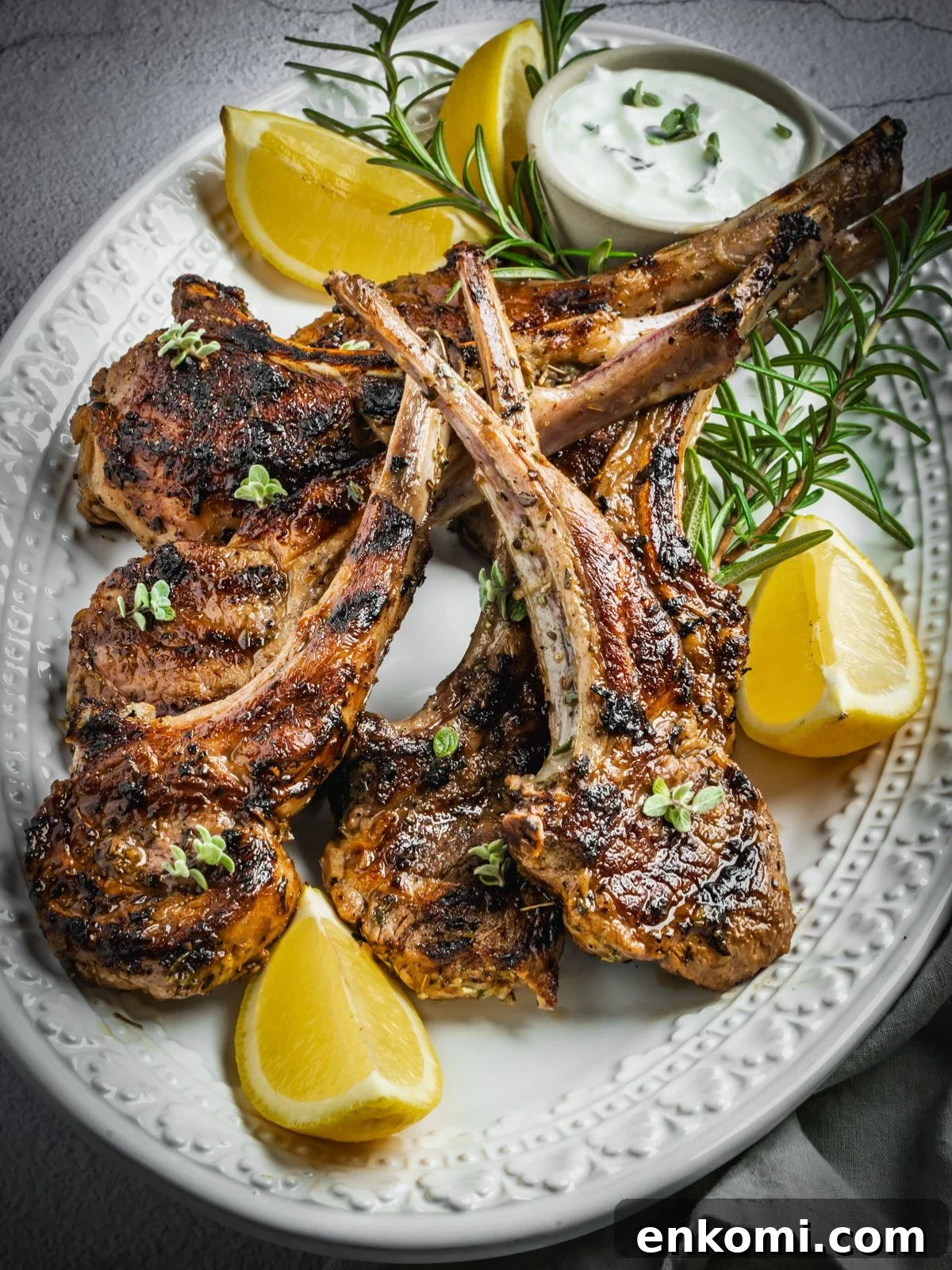 Grilled or Pan-Seared Marinated Greek Lamb Chops 2 Grilled and marinated Greek lamb chops on a platter with rosemary and lemon wedges.