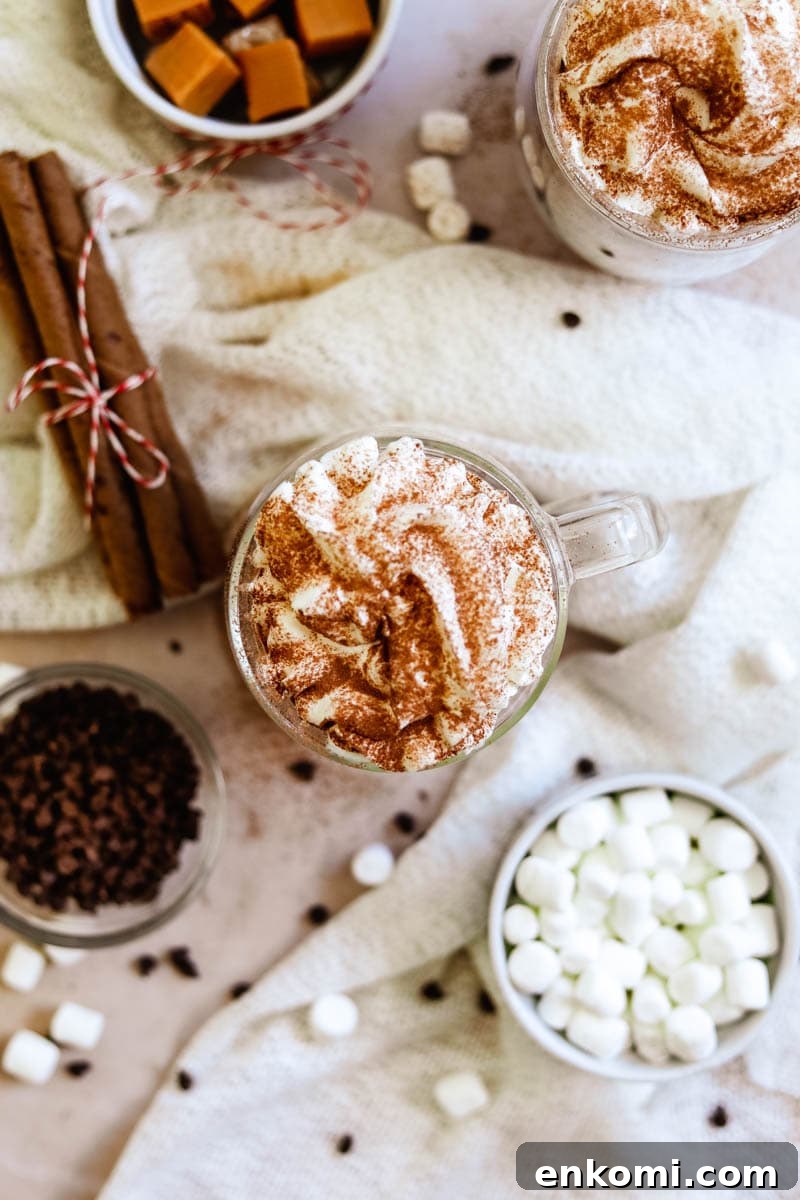 Creamy Oat Milk Hot Chocolate Recipe for Cozy Winter Nights 5 Flatlay image of oat milk hot chocolate in a mug with whipped cream and various toppings, including marshmallows, chocolate chips, and caramels.