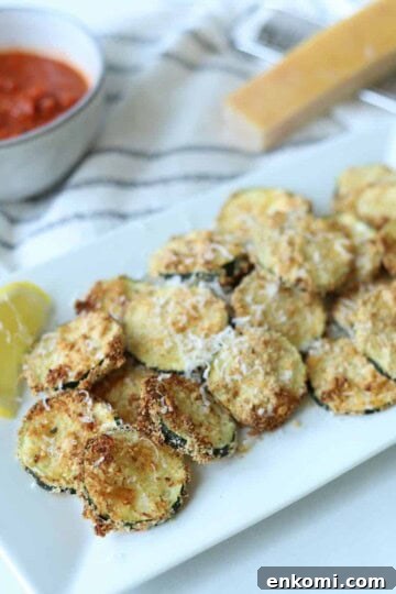 Air fryer zucchini on white plate with lemon wedges and marinara sauce.