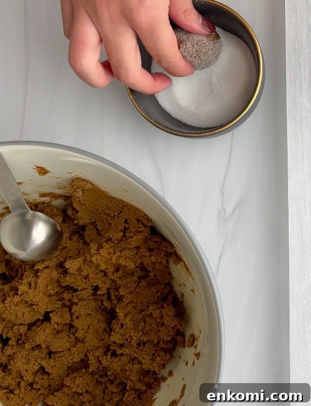 Cookie dough ball being rolled in granulated sugar.