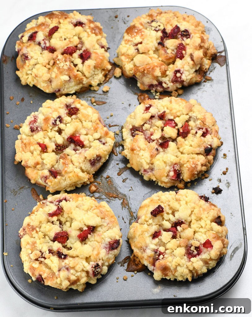 Strawberry Cream Cheese Muffins Recipe — Soft & Lemony 5 freshly baked strawberry cream cheese muffins with crumb topping in muffin pan