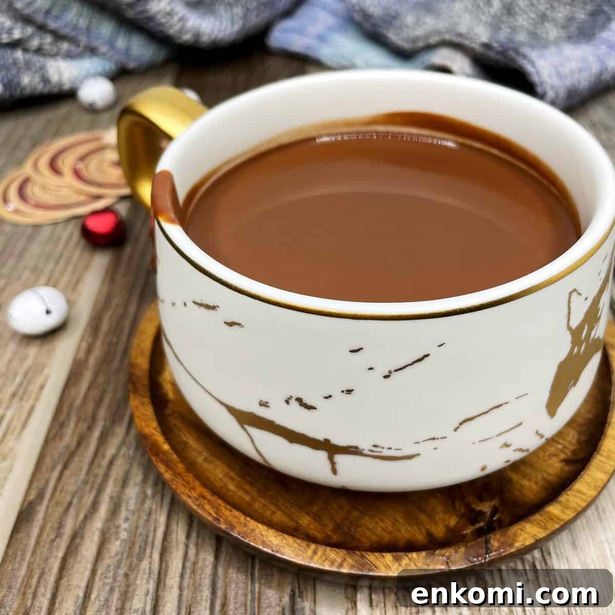 A marble teacup with hot chocolate, Christmas decorations, and tissue in the background.