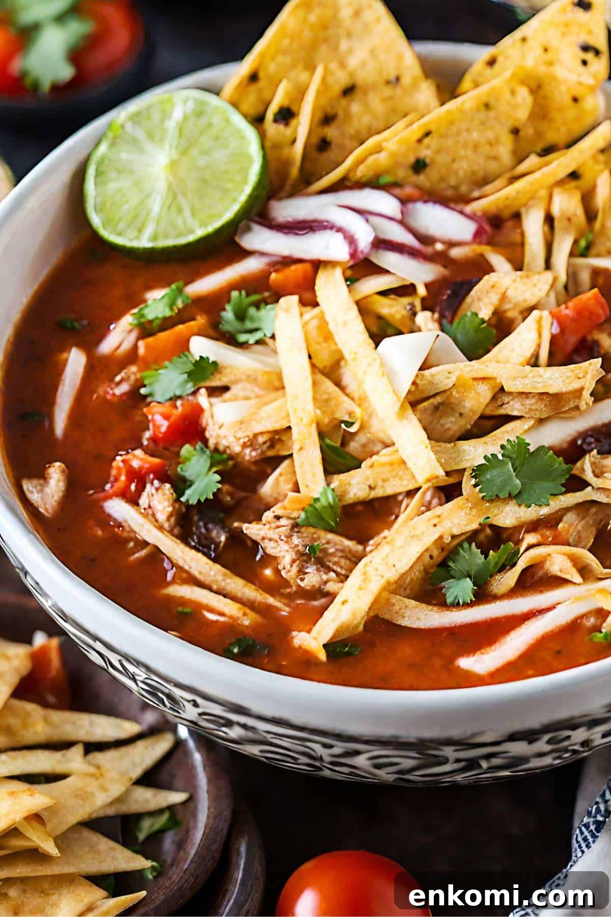 Chicken tortilla soup in a bowl with lime, cilantro and tortilla strips.