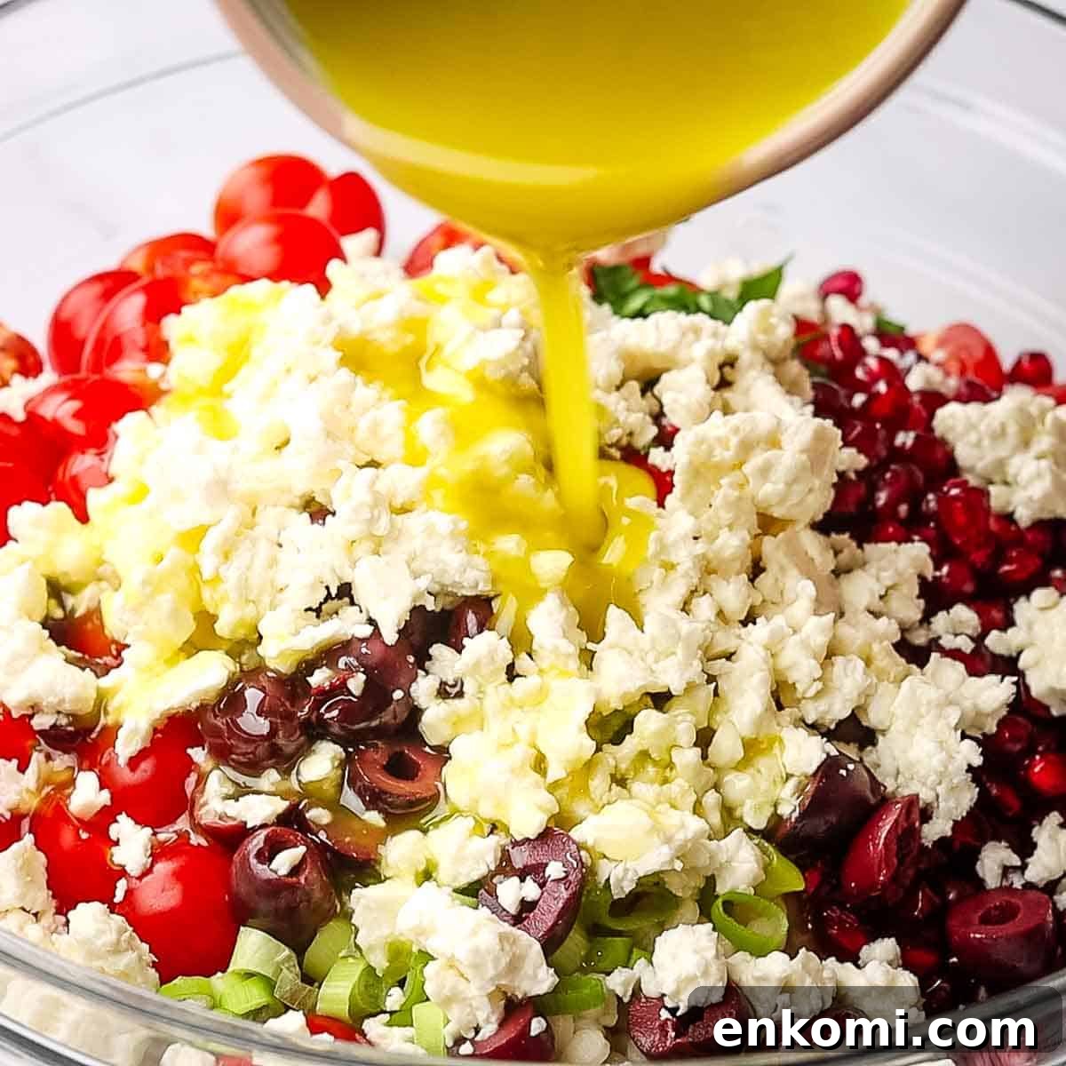 Mediterranean Pearl Couscous Salad with Fresh Herbs & Feta 10 Dressing being drizzled on a bowl of ingredients to make Israeli couscous salad.
