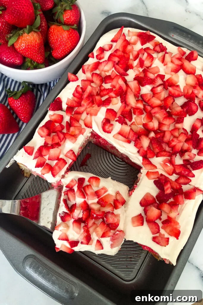 strawberry poke cake with diced strawberries on top and a bowl of strawberries in a bowl
