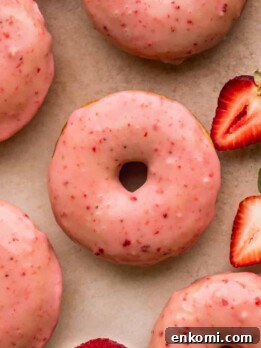 Close up of strawberry glazed donuts with strawberries on the side.