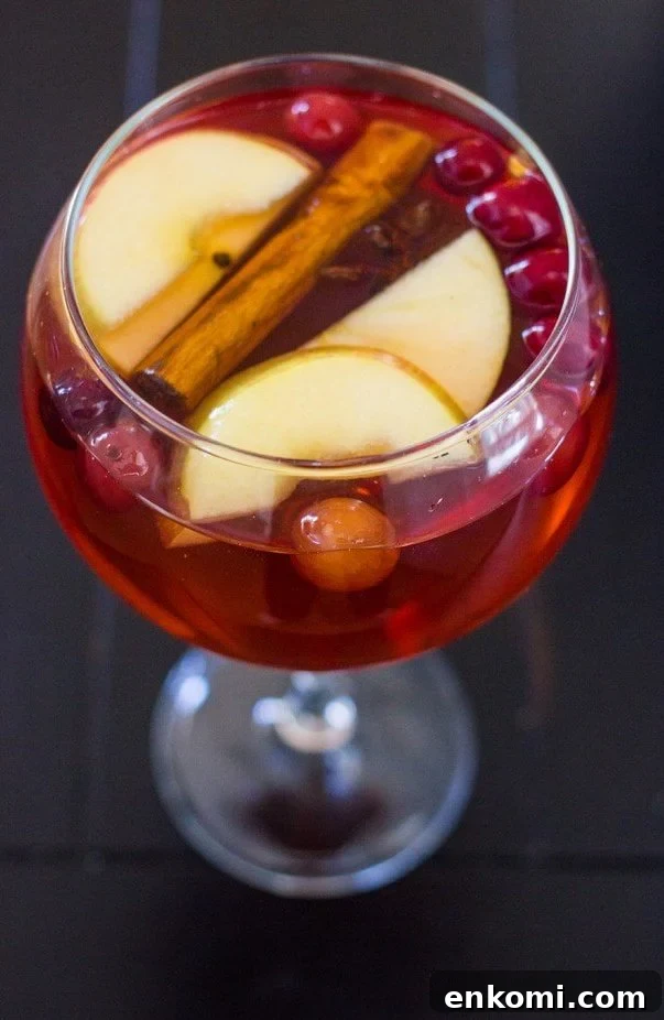 Festive glass of cranberry sangria with apple slices and cinnamon.