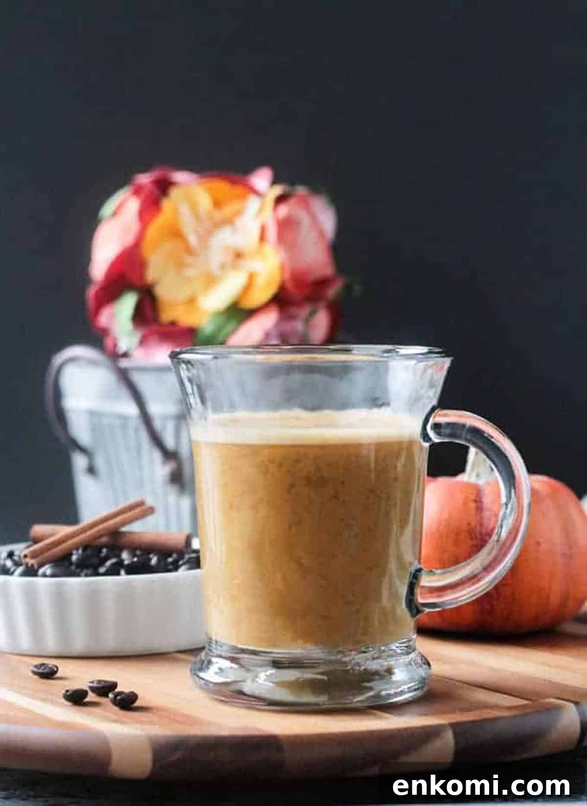 Harvest Oat Pumpkin Latte - a creamy, dairy free coffee drink perfect for sipping this fall. Made with real pumpkin and no refined sugar, this delicious beverage is a indulgent treat you can feel good about. Tastes like your favorite pumpkin spice latte! Pumpkin Latte in a glass with a small metal bucket of flowers in the background.