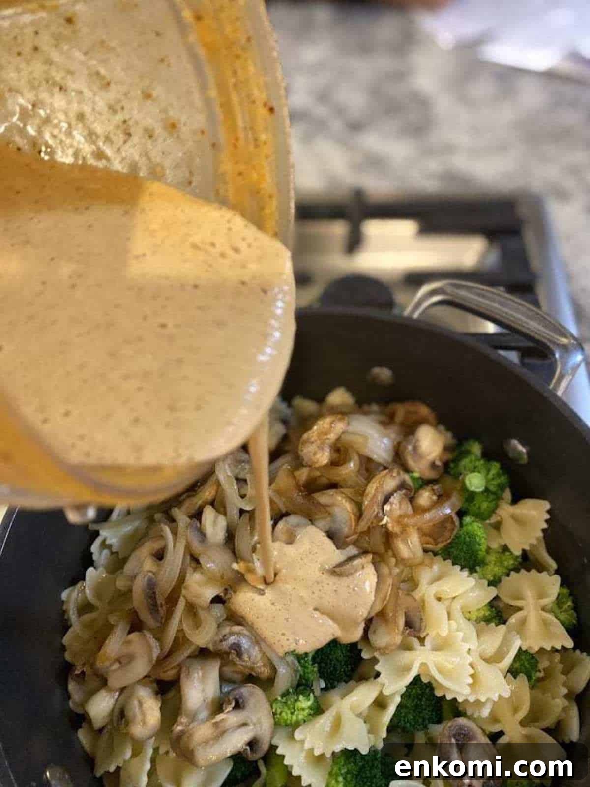 Vegan chipotle cheese sauce in a blender pouring to a pan of cooked ingredients on the stove.
