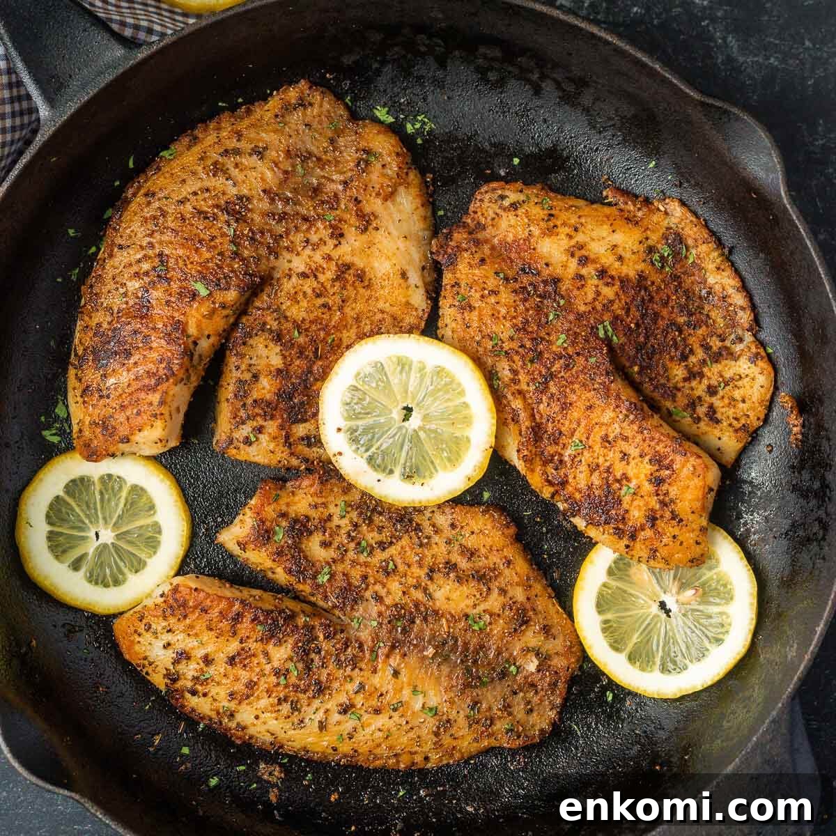 Tilapia in a cast iron skillet with slice lemons on the side