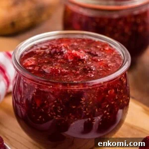 Crockpot Strawberry raspberry jam in glass jar, on top wooden board, bowl of fresh raspberries, bowl of fresh strawberries, red and white striped cloth.