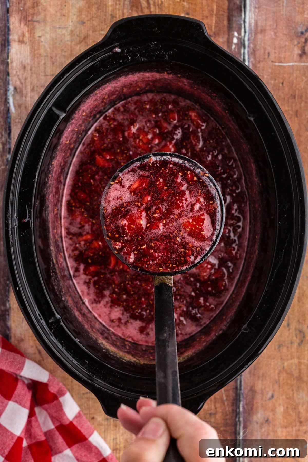 Ladle lifting a big scoop of strawberry raspberry jam from the slow cooker.