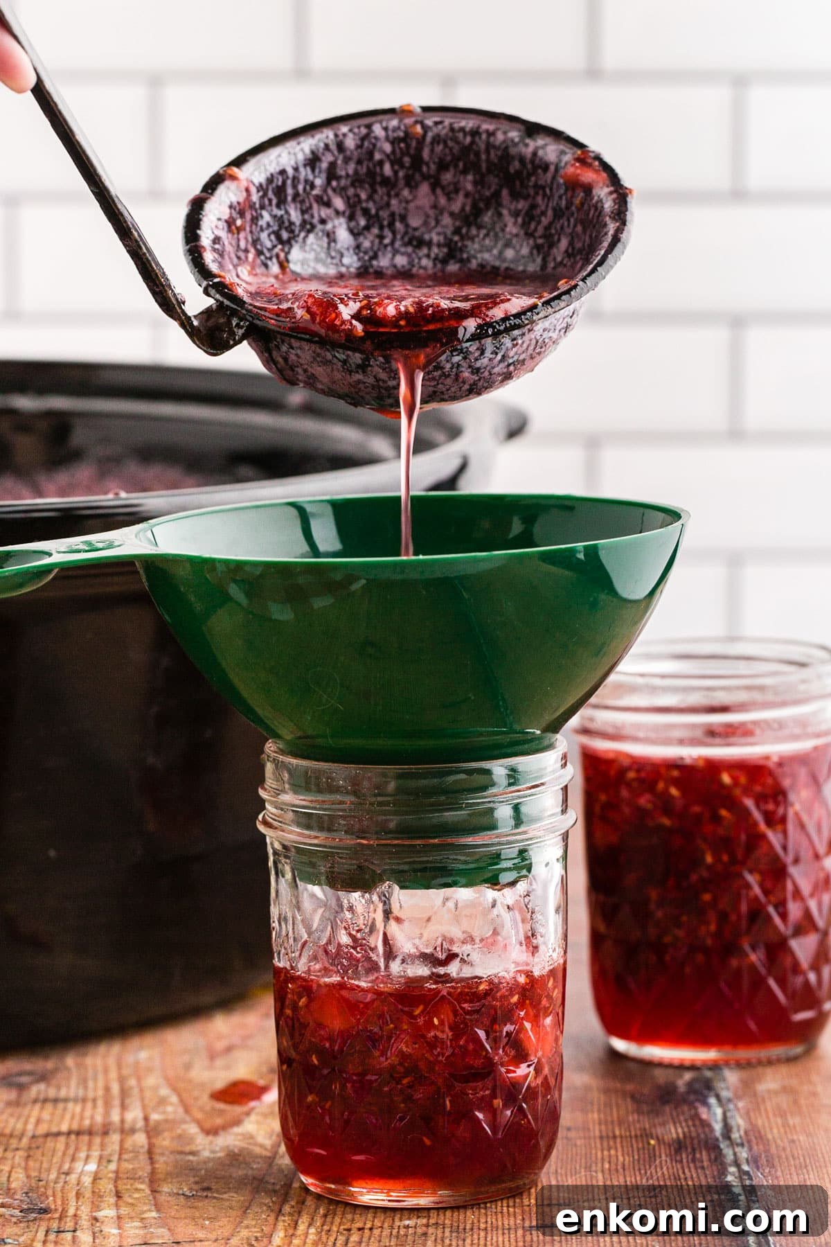 Ladle pouring the strawberry raspberry jam into a jar with the use of a canning funnel placed on top of the jar.