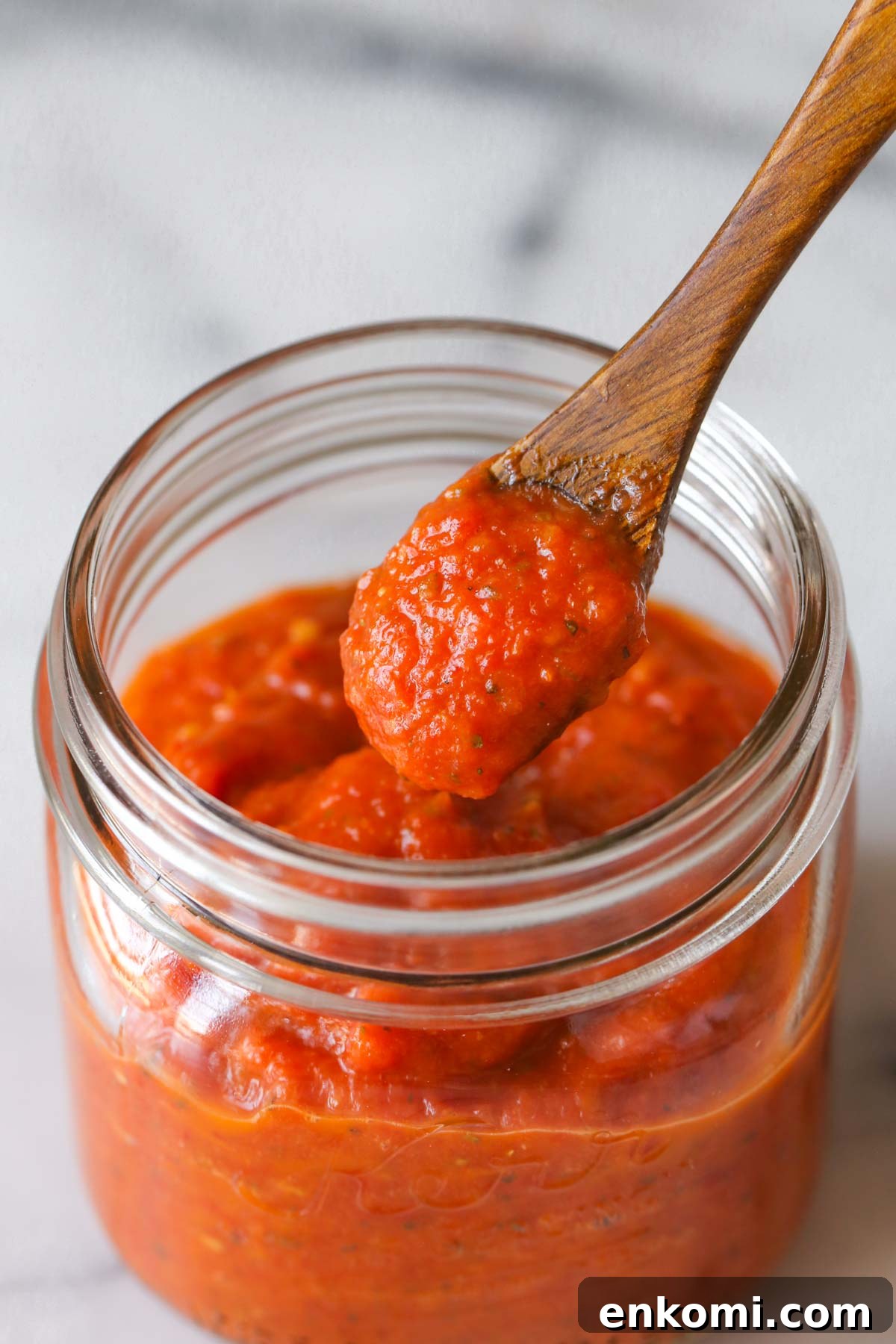 Roasted Tomato Pizza Sauce Recipe for Rich, Smoky Flavor 3 Close up shot of a small wooden spoon full of Roasted Tomato Pizza Sauce that has been scooped out of a jar of Roasted Tomato Pizza Sauce.