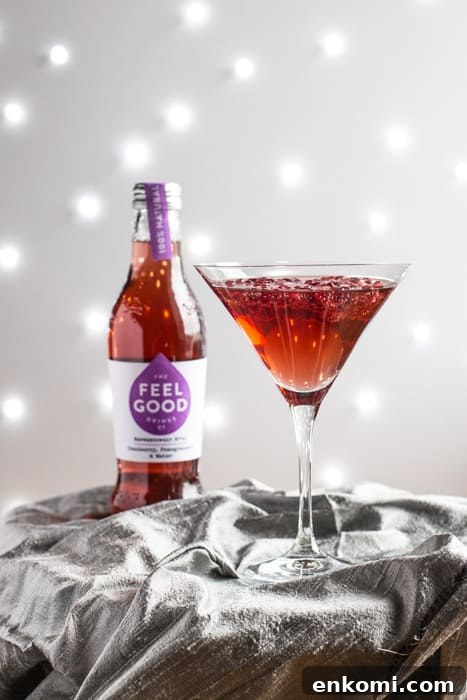 A cocktail glass of Pomagranate Popper Cocktail beside a bottle of Feel Good Cranberry and Pomagranate juice