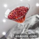 cocktail glass with pomegranate popper cocktail and pomegranate seeds against a sparkly grey background