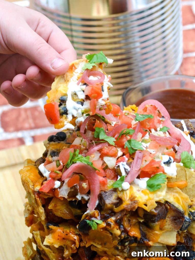 Loaded Nachos: How to Make Trash Can Nachos at Home 6 a hand holding up a loaded chip from a nacho stack