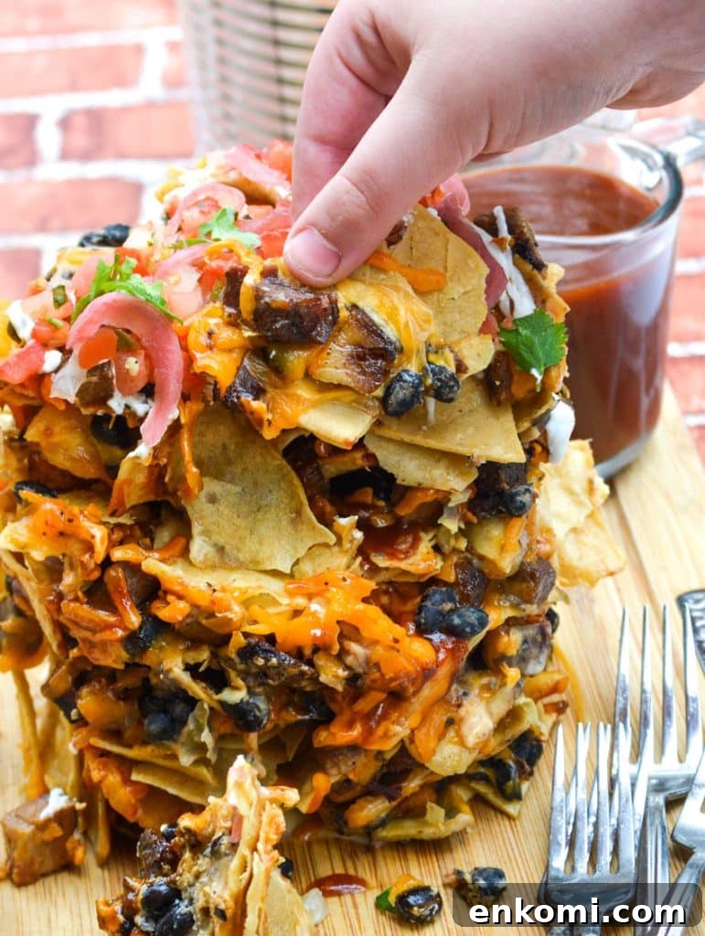 Loaded Nachos: How to Make Trash Can Nachos at Home 7 a hand shown pulling nachos from a stack of cheesy trash can nachos