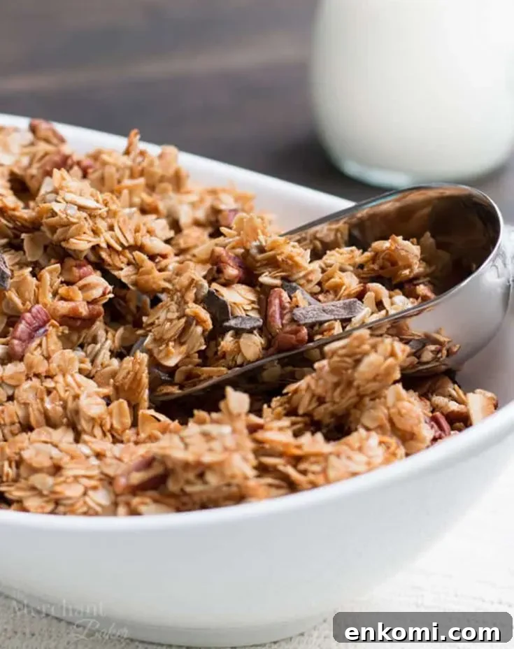 Scooping Chocolate Chunk Pecan Granola out of a bowl by themerchantbaker.com