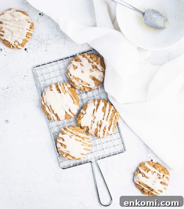 brown butter iced pumpkin cookies on a small silver cooling rack next to a piece of white linen and a bowl.