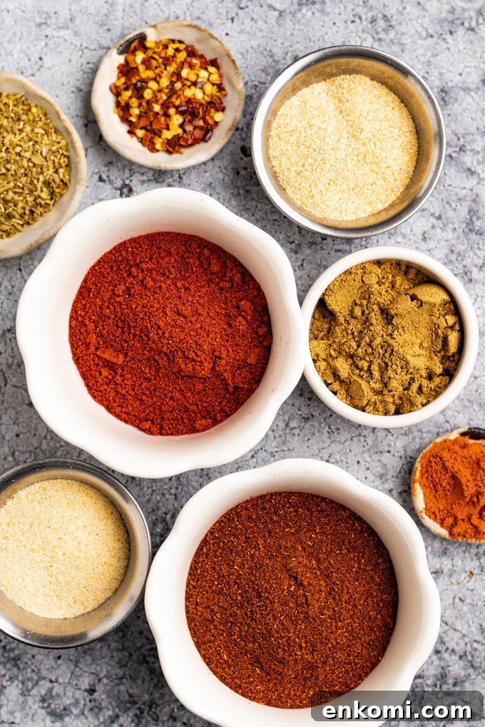 Spices in different bowls - chili powder, smoked paprika, cumin, garlic powder, onion powder, cayenne pepper, dried oregano, and red pepper flakes.