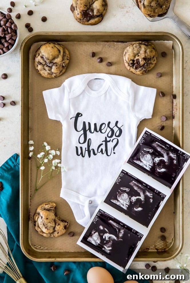 Baby onesie with ultrasound pictures surrounded by cookies and chocolate