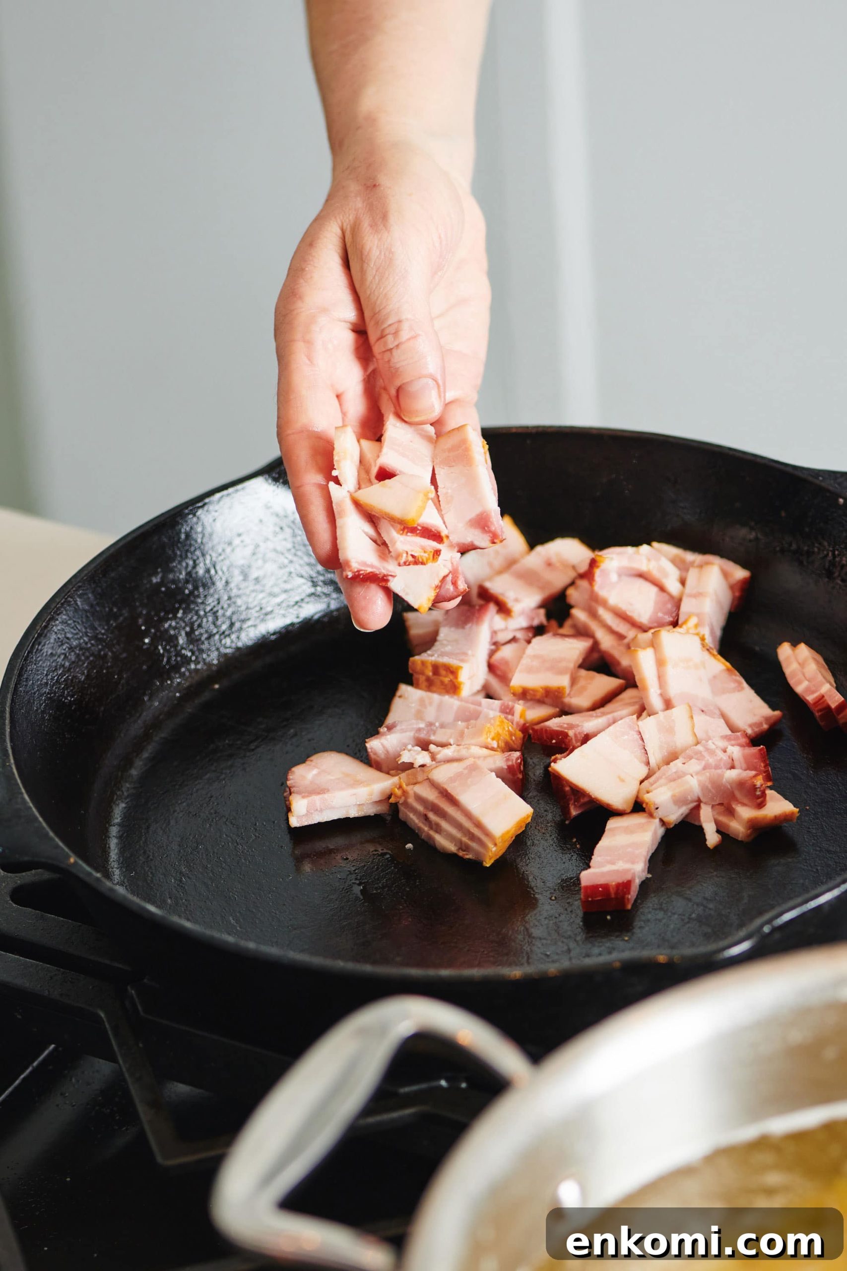 Crispy Bacon Lardons Recipe: Step-by-Step Guide 2 Woman putting uncooked sliced bacon into a cast iron pan.