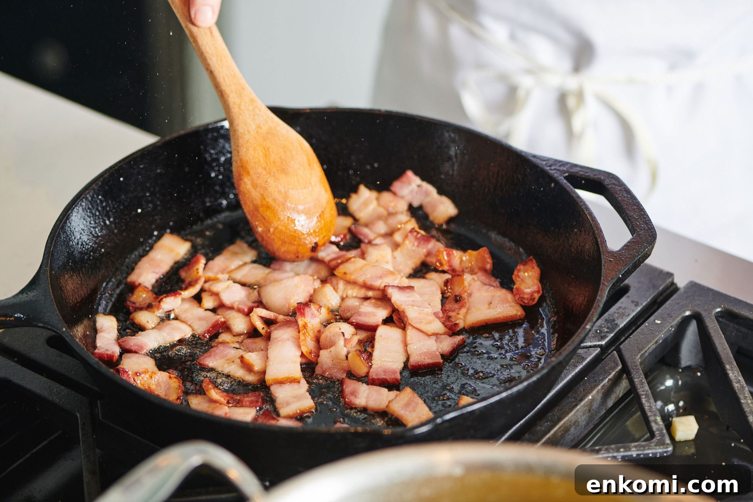 Crispy Bacon Lardons Recipe: Step-by-Step Guide 4 Spoon stirring Bacon Lardons in a cast iron pan.