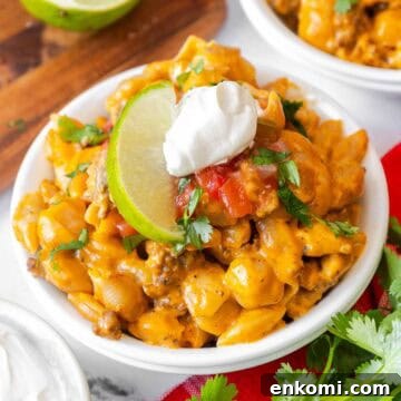 Small white bowl filled with taco mac and cheese, garnished with sour cream, salsa, chopped cilantro, and a lime slice.