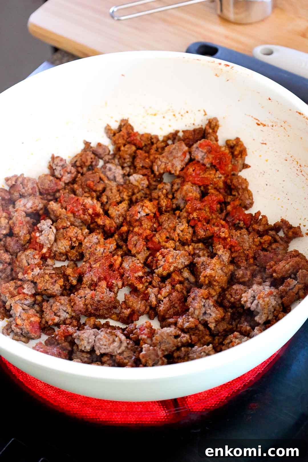 Seasoned ground beef cooking in a skillet with visible tomato paste mixed in.