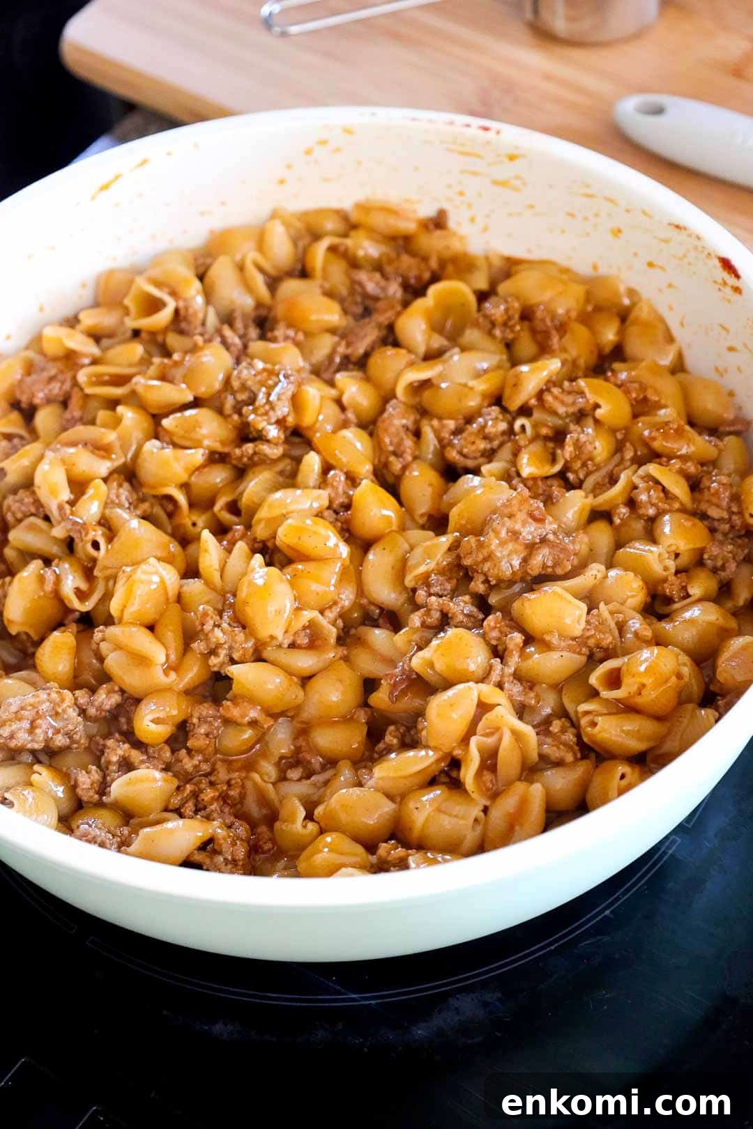 Pasta shells and seasoned beef just combined in the skillet before the cheese is fully melted.