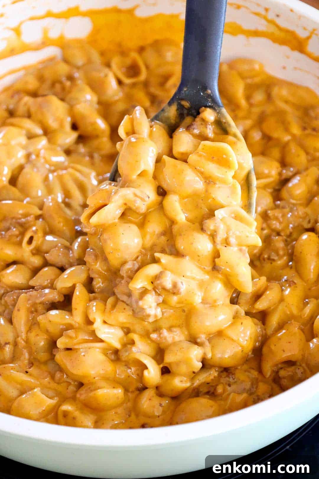 A large spoon lifting a serving of creamy taco mac and cheese out of the pan, showing melted cheese coating the shell pasta and beef.