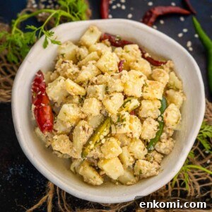 Sesame Potato Stir-Fry (Til Wale Aloo) Recipe 12 A bowl of Til Wale Aloo garnished with sesame seeds, red and green chilies, and fresh cilantro, set on a rustic surface with scattered chilies and herbs around.