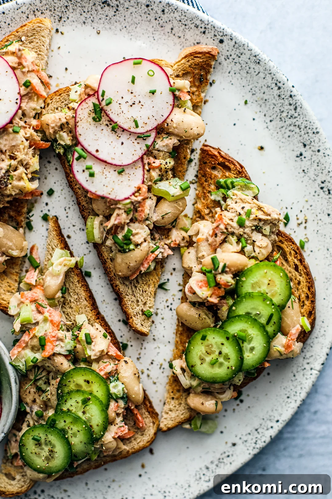 Overhead close up of fancy toasts topped with mackerel and white bean salad, radishes, and cucumbers.